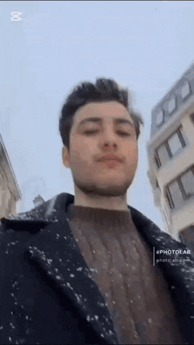 a young man is standing in front of a building with snow on his coat .