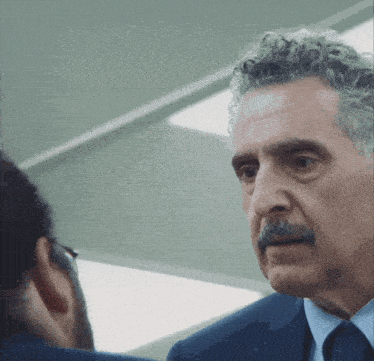 a man with curly hair and a mustache is wearing a blue suit and tie