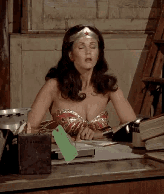wonder woman is sitting at a desk with her eyes closed and her breasts exposed .