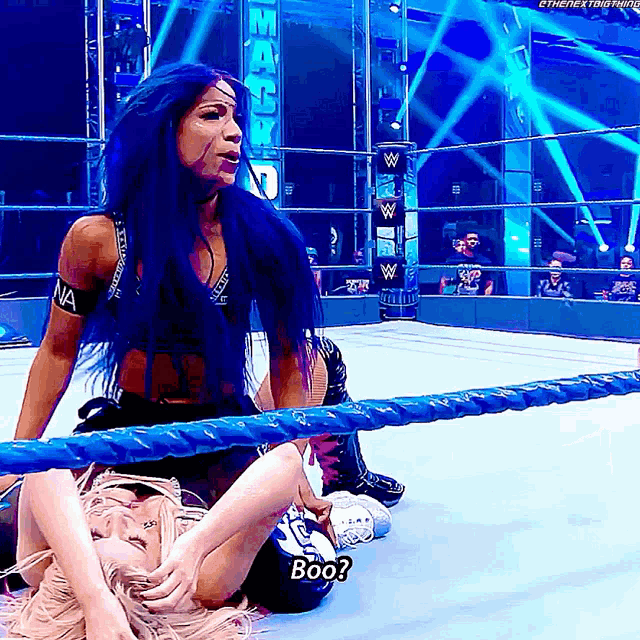 a woman with blue hair is sitting in a wrestling ring talking to another woman