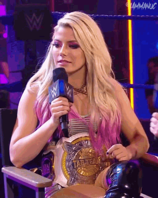 a woman in a wrestling ring is holding a microphone and wearing a championship belt with the word tag team on it