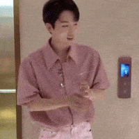 a man in a pink shirt is standing with his arms crossed in front of a door .