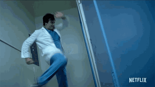 a man in a lab coat and scrubs is jumping in a hallway with a netflix logo behind him