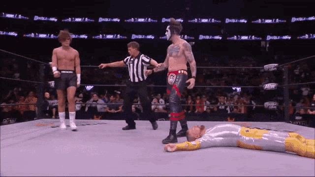 a wrestler is laying on the ground in a wrestling ring while a referee looks on