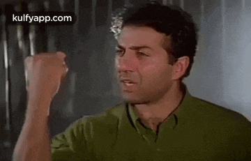 a man in a green shirt is holding his fist up .