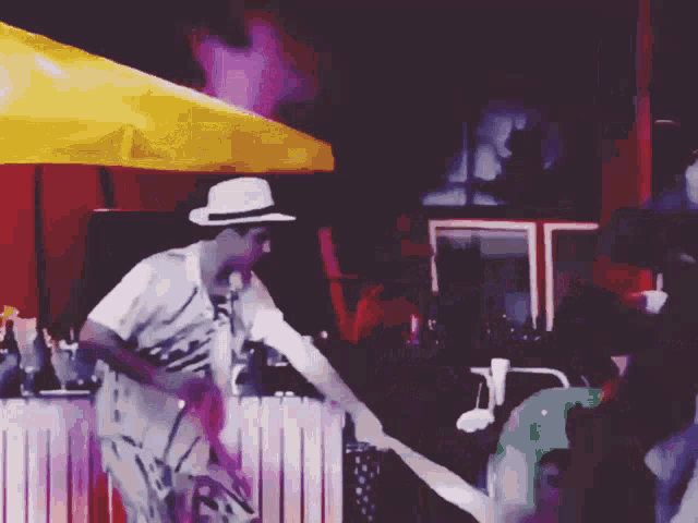 a man in a white hat is standing under a yellow umbrella in a dark room