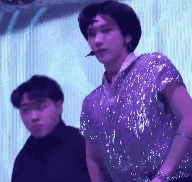 a man in a sequined shirt is standing next to another man in a black turtleneck .