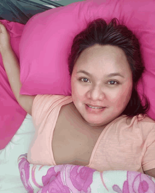 a woman laying on a bed with a pink pillow and a purple blanket