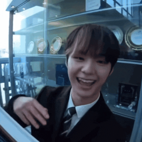 a young man in a suit and tie is smiling in front of a glass display case