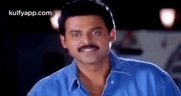 a man with a mustache is wearing a blue shirt and looking at the camera .