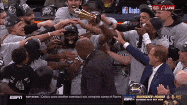 a group of basketball players celebrate with a trophy in front of a espn advertisement