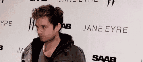 a man in a black jacket is standing in front of a white wall with the word jane eyre on it .