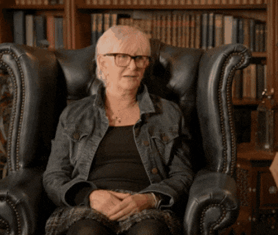 a woman wearing glasses is sitting in a chair in front of a bookshelf