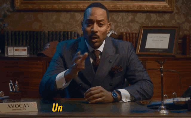 a man in a suit and tie sits at a desk with a sign that says avocat