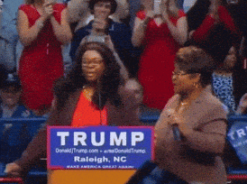 a woman is standing in front of a trump sign in raleigh nc