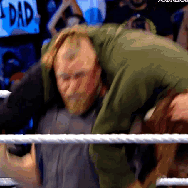 a man is carrying another man in a wrestling ring with a sign that says dad behind him