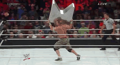 a man in a wrestling ring is holding a giant m in front of a crowd