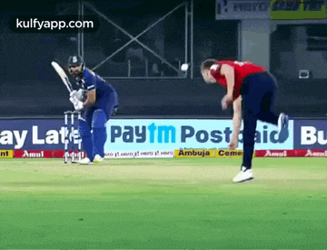two cricket players are playing a game of cricket on a field sponsored by paytm post aid .
