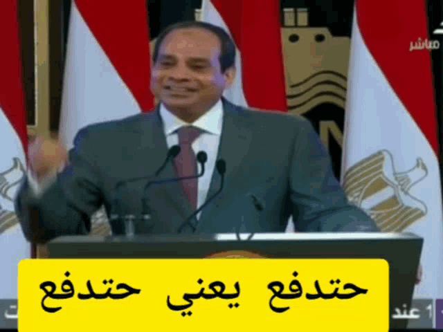 a man in a suit and tie is giving a speech in front of microphones and flags