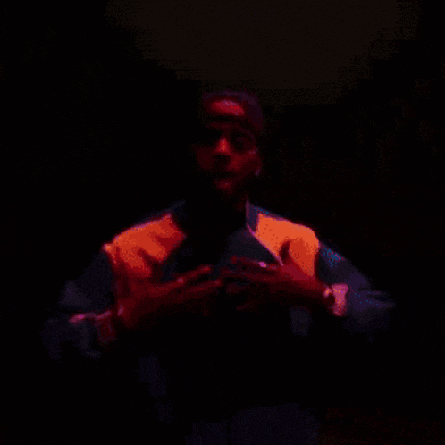 a man wearing a red hat and a purple jacket is standing in a dark room .