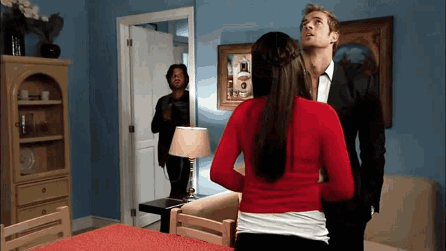 a woman in a red sweater stands next to a man in a suit in a living room