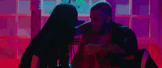 a man and a woman are kissing in a dark room with a purple light behind them .