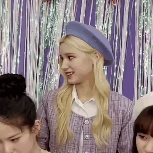 a blonde woman wearing a blue hat and a purple jacket