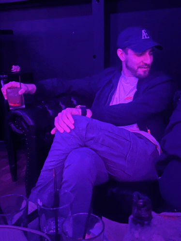a man wearing a hat with the letter a on it sits in a dark room