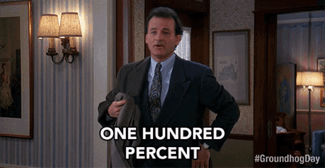 a man in a suit and tie is standing in a hallway and says one hundred percent