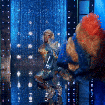 a drag queen is dancing on a stage in front of a waterfall of lights