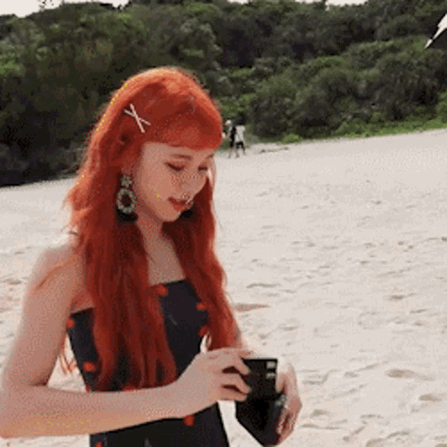 a woman with red hair is standing on the beach holding a camera
