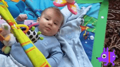 a baby laying on a play mat with a purple hedgehog behind him