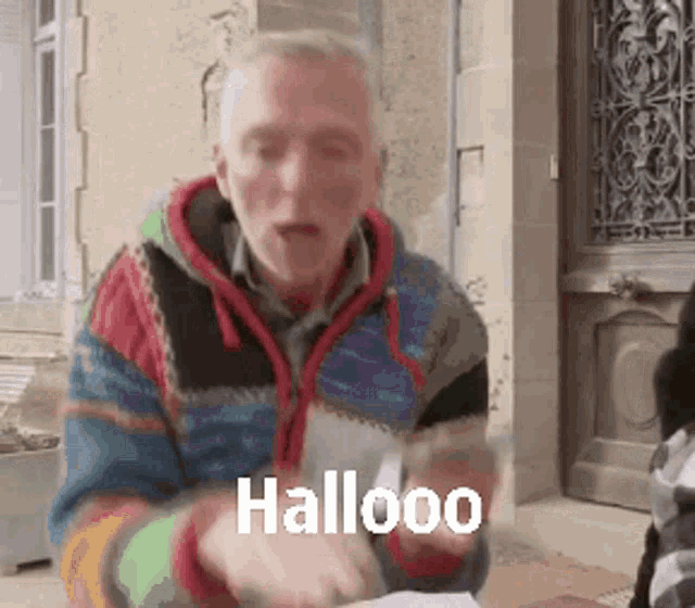 a man in a colorful sweater is standing in front of a building with the word halloo written on it .