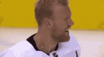 a man with a beard is wearing a white hockey jersey and laughing .