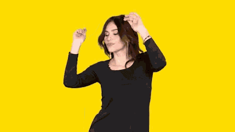 a woman in a black dress is dancing with her arms in the air against a yellow background .