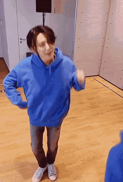 a man in a blue hoodie is dancing in a room