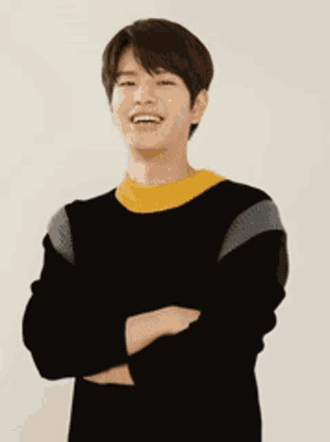 a young man wearing a black and yellow sweater is smiling with his arms crossed .