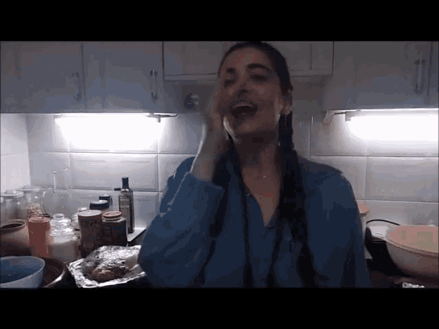 a woman in a blue shirt is standing in a kitchen with a foil container of food