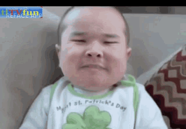 a baby is crying with his eyes closed and wearing a shamrock bib .