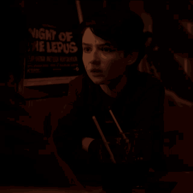a woman sits at a table in front of a poster that says night of the lepus