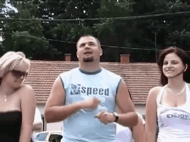 a man in a blue shirt with the word speed on it is standing next to two women .