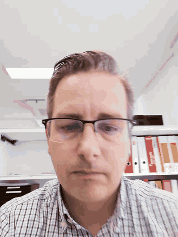 a man wearing glasses and a plaid shirt is standing in front of a row of binders with the word microsoft on them