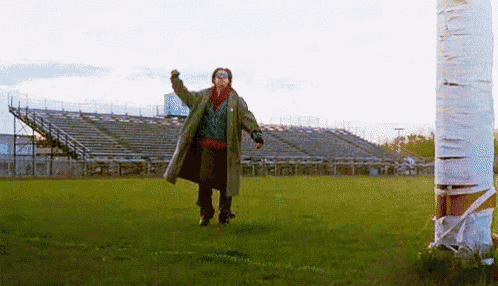 a man in a trench coat is standing in a field with his arms outstretched .