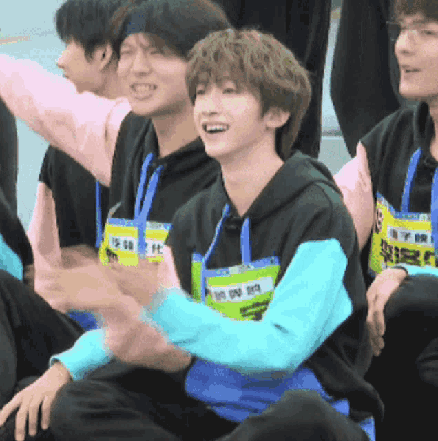 a group of young men are sitting in a row and one of them has a yellow lanyard around his neck with chinese writing