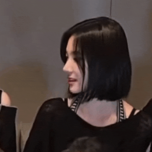 a woman with short black hair is wearing a black top and a bra .