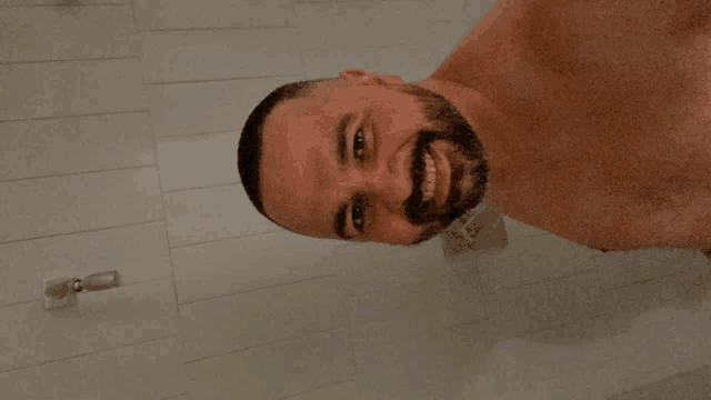 a shirtless man with a beard smiles in a shower