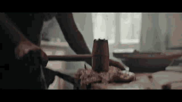 a person is hammering a piece of meat on a cutting board with a wooden hammer .