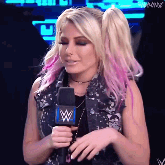 a woman with blonde and pink hair is holding a microphone with a w logo on it .