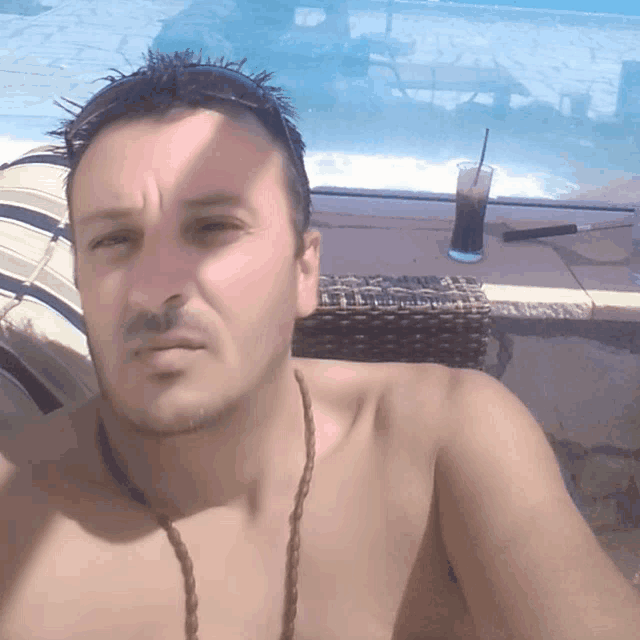 a shirtless man takes a selfie with a drink in the background