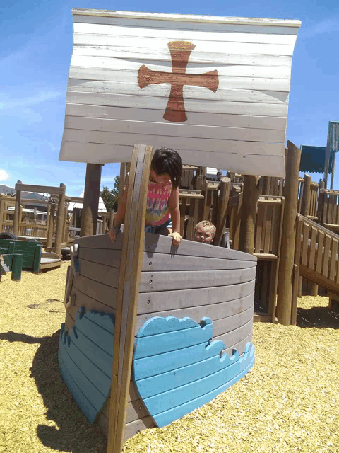 a little girl in a pink shirt is playing in a wooden boat